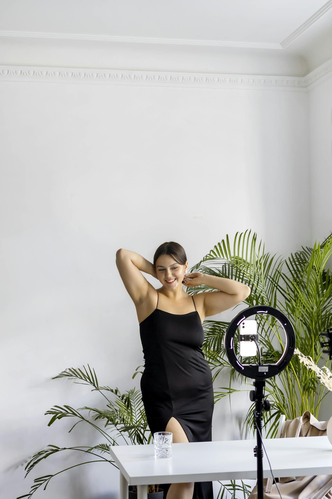 Young woman posing joyfully indoors with a camera setup, embodying modern lifestyle.